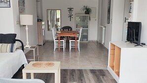 A modern living room with a sofa, a coffee table, and a TV on a stand. There is a dining area with a table and chairs. - Comfortable, quiet "CôtéPlage" gîte-Covered terrace-Garden  (Vaux-Sur-Mer)