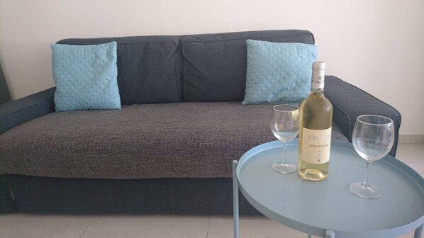 Un canapé gris foncé agrémenté de deux coussins bleu clair, une bouteille de vin et deux verres à vin vides, le tout posé sur une petite table ronde.