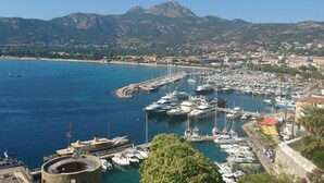 Un port de plaisance où sont amarrés de nombreux bateaux, entouré d’une ville côtière et avec des montagnes en arrière-plan.