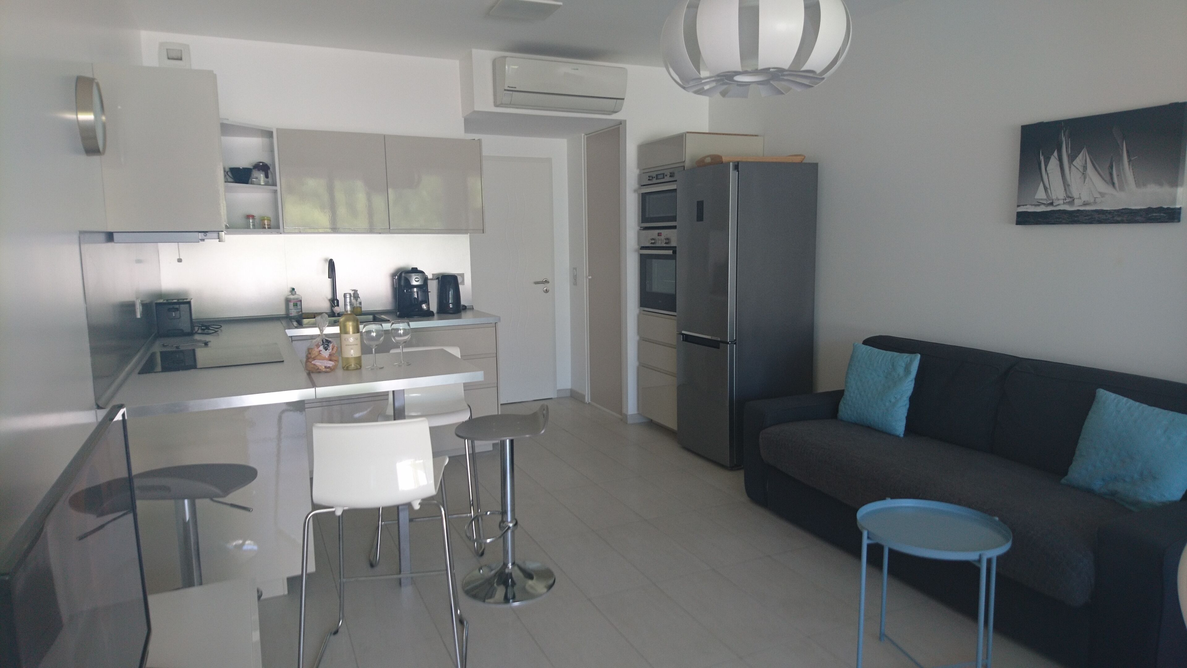 A modern kitchen with a central island, a refrigerator, and a dining area with stools.