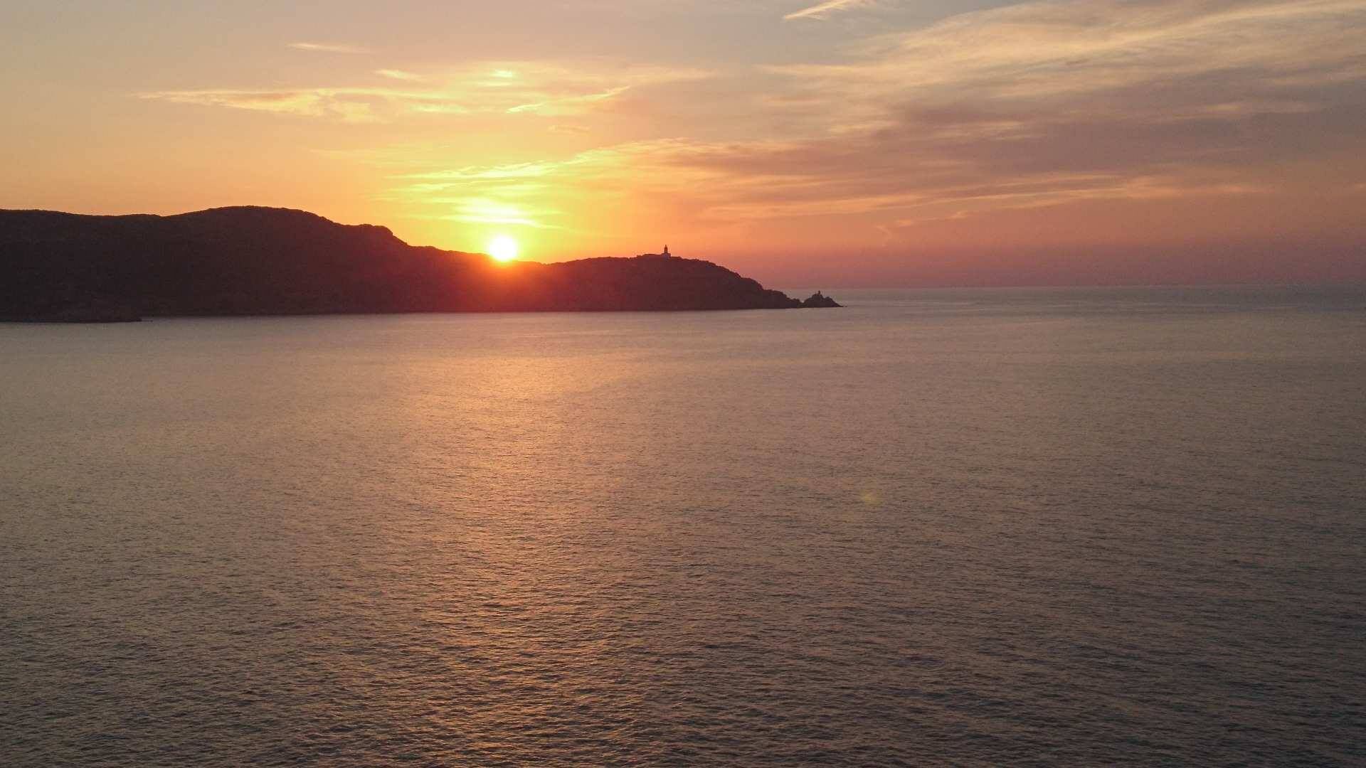 Ein Küsten-Sonnenuntergang mit ruhigem Wasser, das den Himmel spiegelt.