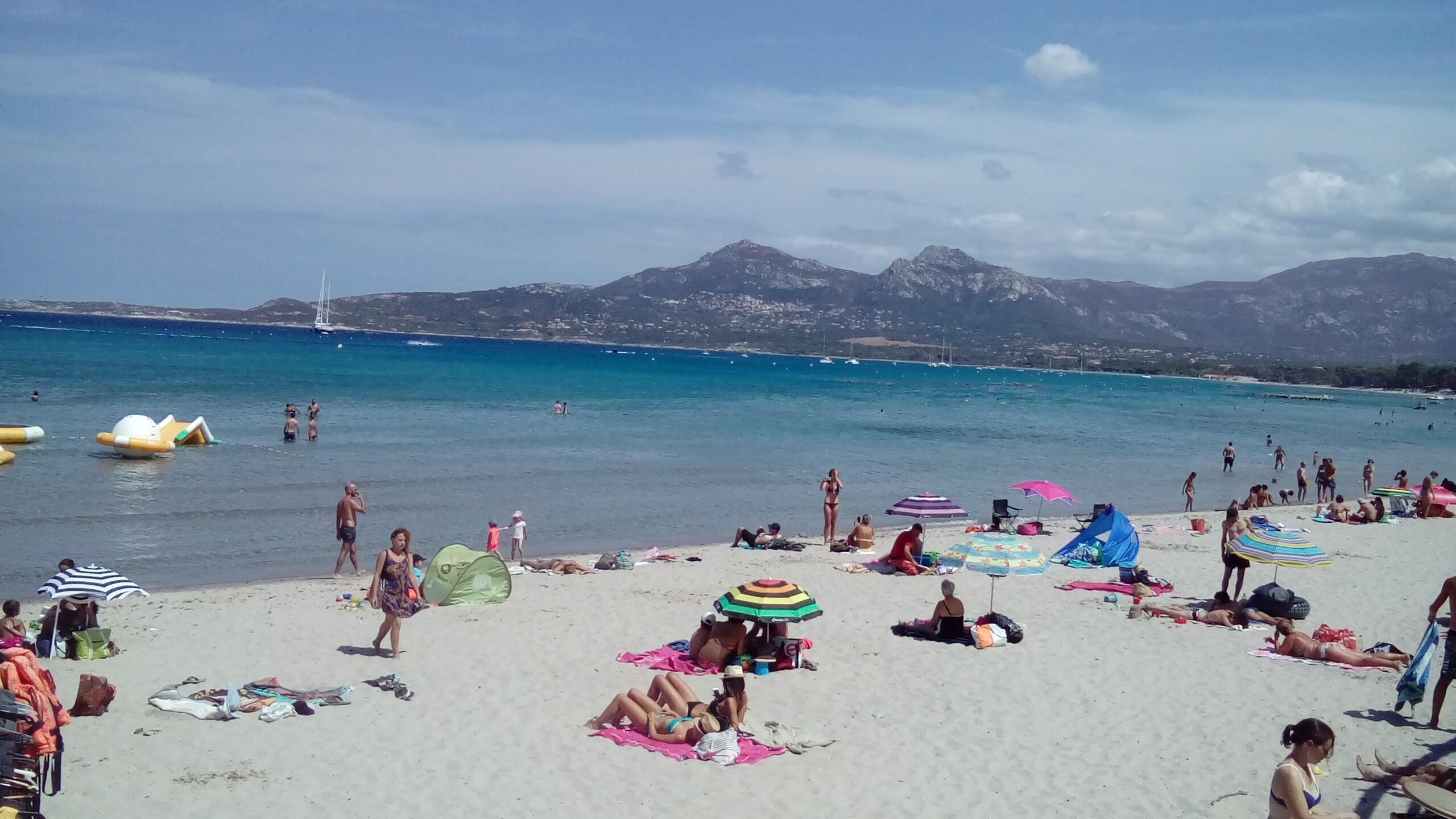 Una spiaggia affollata con persone che prendono il sole e nuotano, ombrelloni e sdraio.