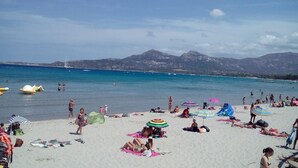 Une plage bondée où les gens se prélassent au soleil et se baignent, avec des parasols et des chaises de plage.