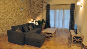 Uma sala de estar aconchegante com parede de pedra, escada de madeira, sofá cinza, mesa de centro de madeira e TV sobre suporte de madeira.
