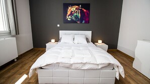 A modern bedroom with a large bed, white bedding, and a colorful abstract painting on the wall.