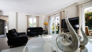 A modern living room with a black sofa, a glass coffee table, and a large TV.