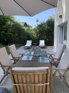 Une terrasse extérieure avec une table en bois prévue pour quatre personnes, entourée de chaises rembourrées, et protégée par un grand parasol.