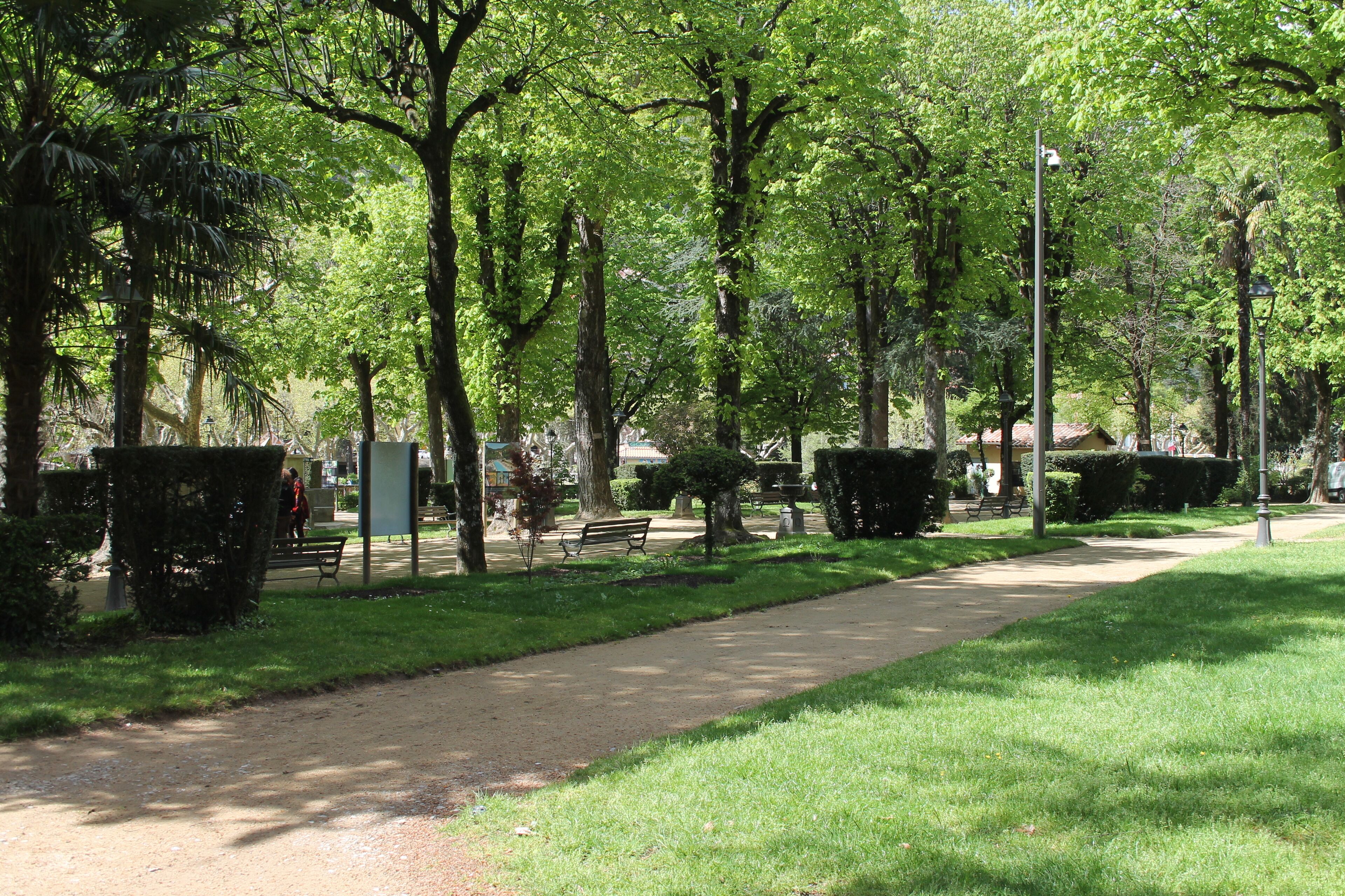 A park with a paved walkway, benches, and trees.