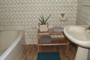 Ein Badezimmer mit einer Badewanne, einem Waschbecken, einer Holzablage mit einer Pflanze und einer kleinen Ablage mit einem Dekorationsgegenstand.