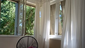 Huoneessa on suuri ikkuna, tuoli, pöytä, jossa on maljakko, ja lehti lattialla.