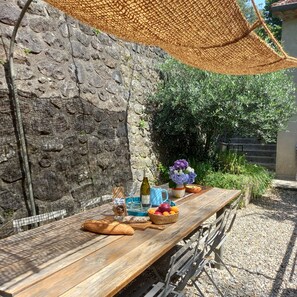 Ein Holztisch mit Brot, einer Flasche, einer Kanne, einer Fruchtschale und einem Blumenstrauß.