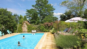 A swimming pool with two people in the water, surrounded by a garden with various plants and a wooden structure. - Dordogne Valley, 4 * holiday house, exclusive pool, 12kms from Bergerac (Bergerac)