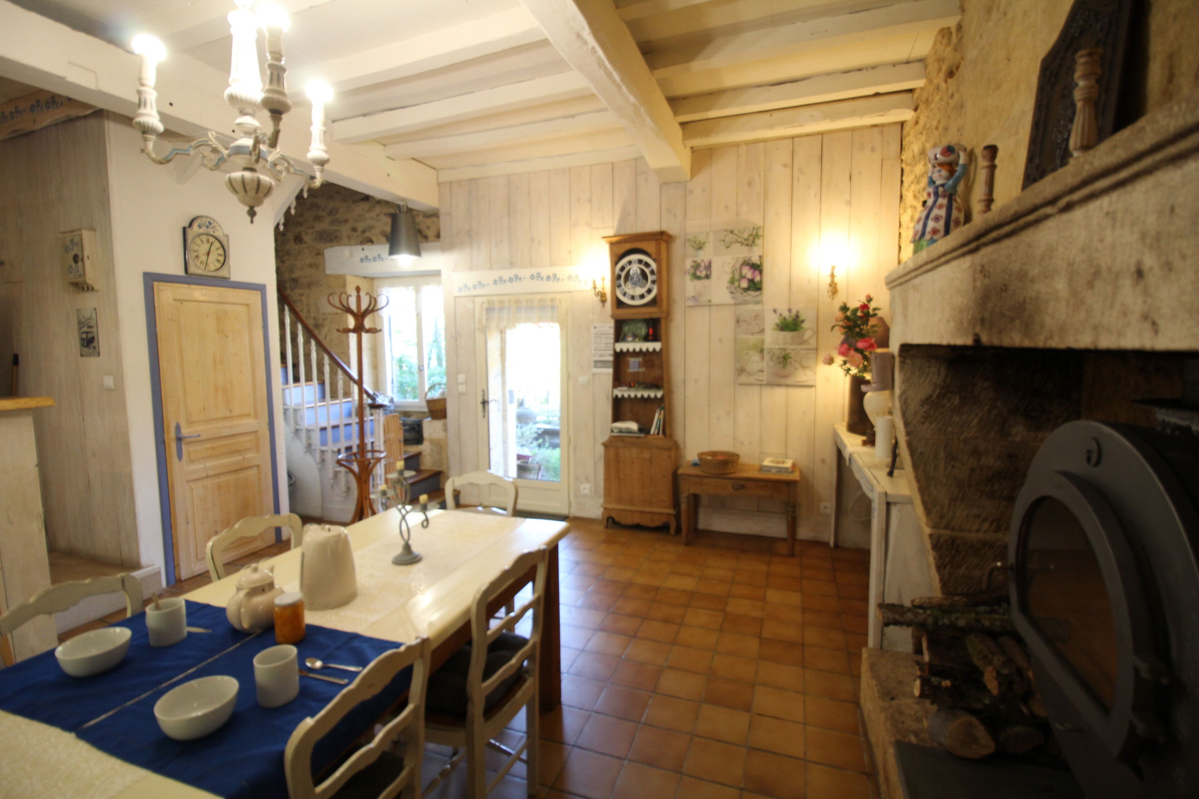 Une cuisine rustique aux murs en bois, une table à manger dressée avec de la vaisselle, une horloge et une cheminée.