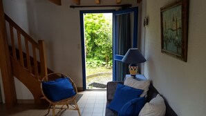 Une pièce avec un escalier en bois, une chaise en osier avec des coussins bleus, un canapé avec des coussins bleus et blancs, une table avec une lampe et un tableau accroché au mur.