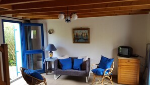 Une pièce confortable avec un canapé, deux fauteuils, une petite table, une lampe, un tableau et un téléviseur.