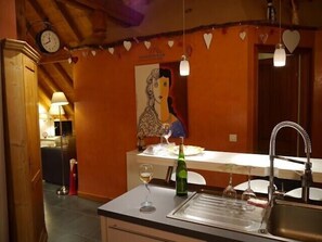 Una cocina con techo de madera, un reloj, adornos con forma de corazón, un cuadro y un lavamanos con copas de vino.