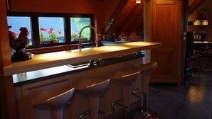 A kitchen with a bar area, wooden ceiling beams, and a window with flowers.