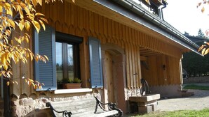 A wooden house with a porch, a bench, and a stone wall.