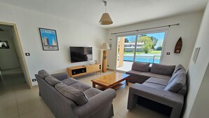 A modern living room with a sofa set, a coffee table, a TV, and a large window with a view of a swimming pool.