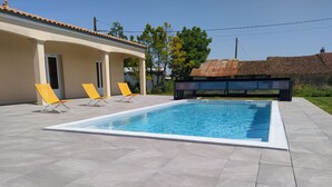 A rectangular swimming pool with a tiled deck, two yellow lounge chairs, and a covered area with a door.