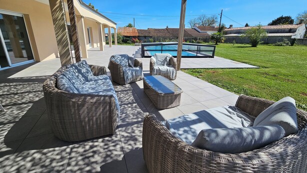 A covered outdoor seating area with wicker furniture, a swimming pool, and a well-maintained lawn.