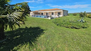 A house with a swimming pool, surrounded by a well-maintained lawn and a few trees.