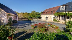 A stone building with a sloped roof, a paved driveway, and surrounding greenery. - Charming cottage and nature, 18 ha, Périgord Noir-Dordogne -Lot -PISCINE and private SPA (Orliaguet)