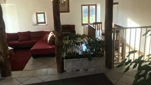 A cozy living room with a red sofa, a wooden tree trunk, and a white decorative planter with green plants. - Charming cottage and nature, 18 ha, Périgord Noir-Dordogne -Lot -PISCINE and private SPA (Orliaguet)