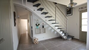 Een moderne trap met glazen balustrade, een hanglamp en een ingelijst schilderij aan de muur.