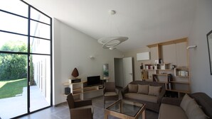 Een ruime woonkamer met een grote schuifpui naar een tuin, een moderne kroonluchter en ingebouwde boekenkasten.