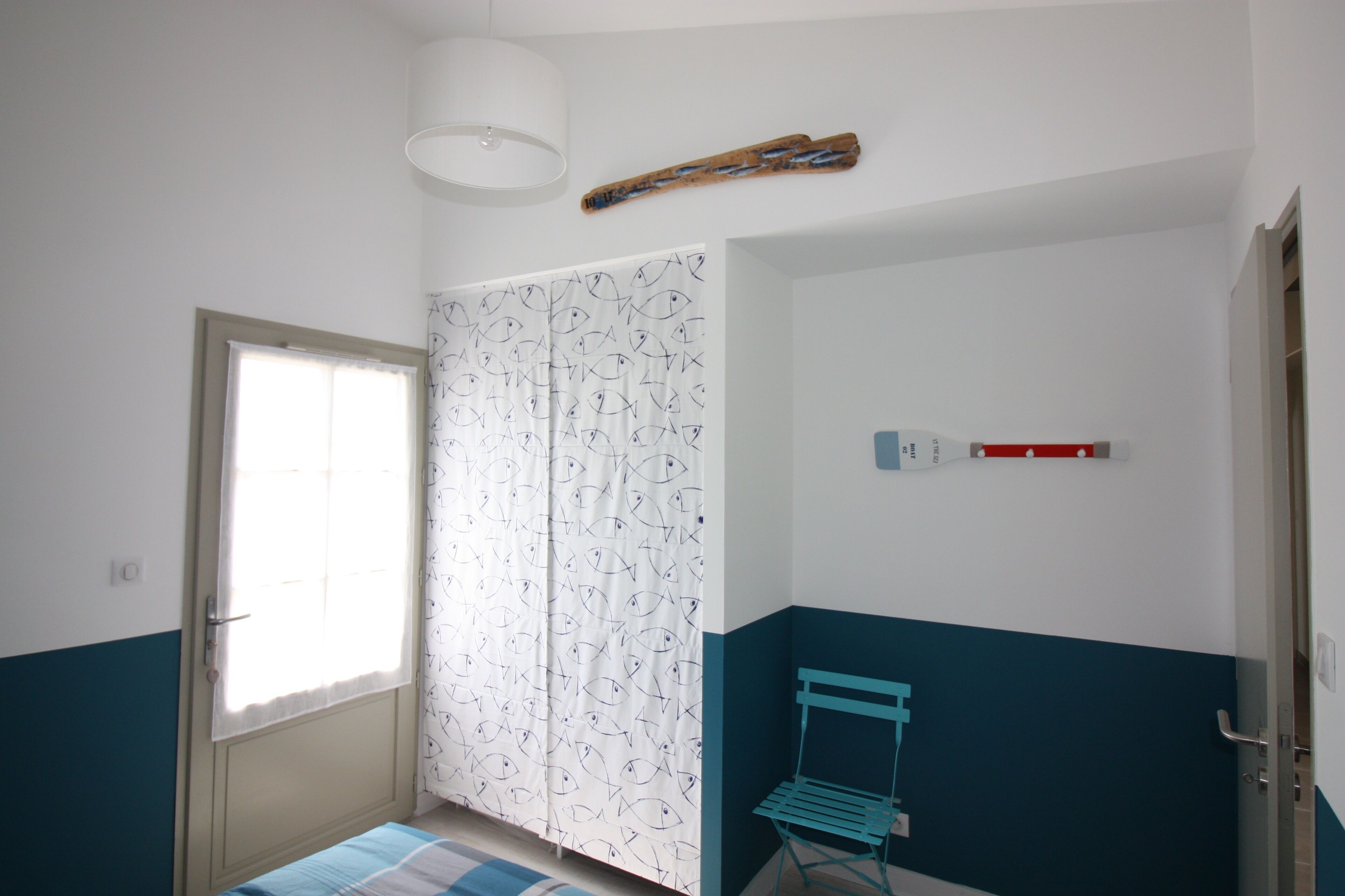 Een kamer met een bed, een raam met gordijnen, een stoel en een wandlamp.