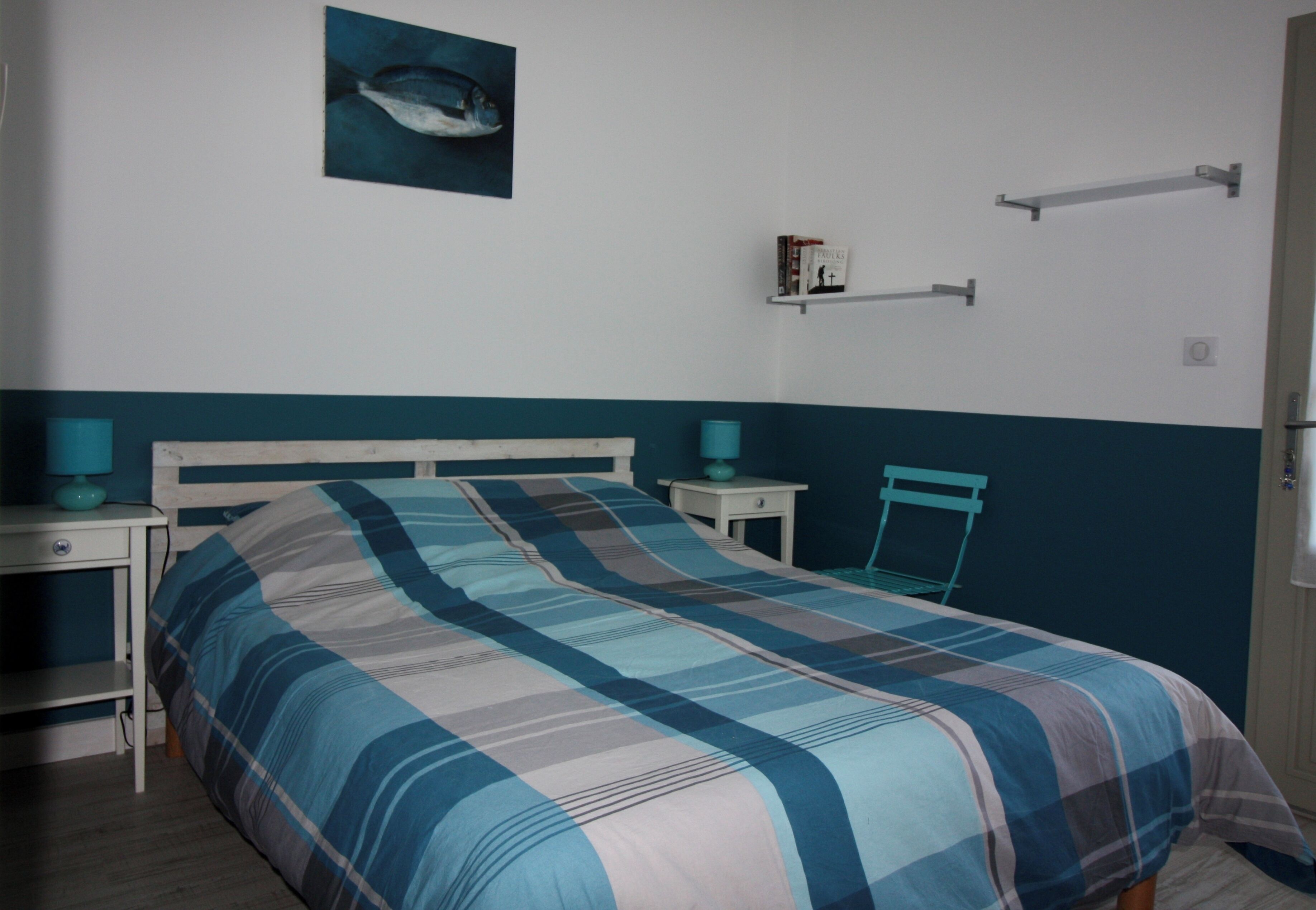 Een slaapkamer met een bed, twee nachtkastjes, een stoel, een plank met boeken en een wandrek voor handdoeken.