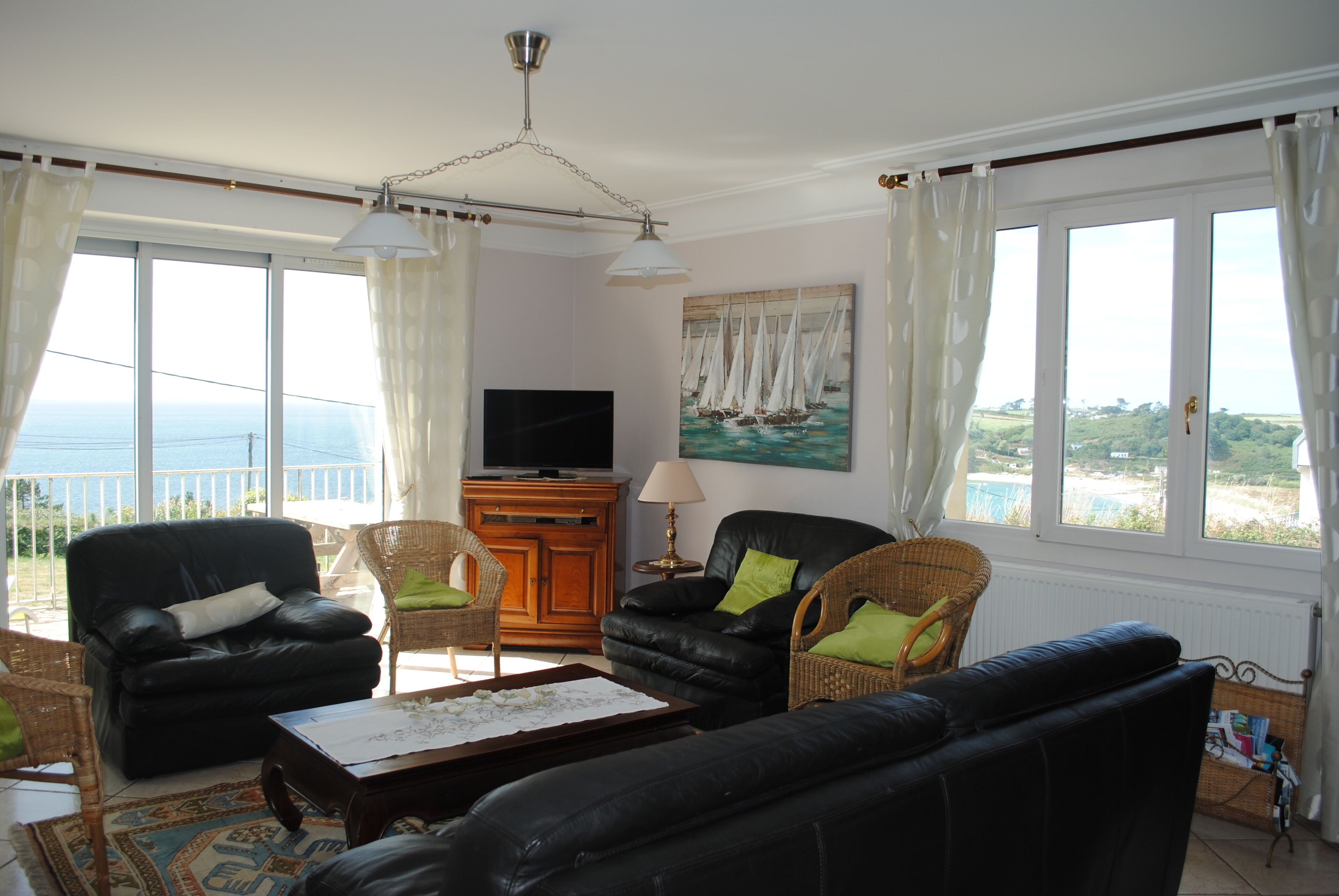 A living room with a black leather sofa, a wooden cabinet, a television, and a painting of sailboats.