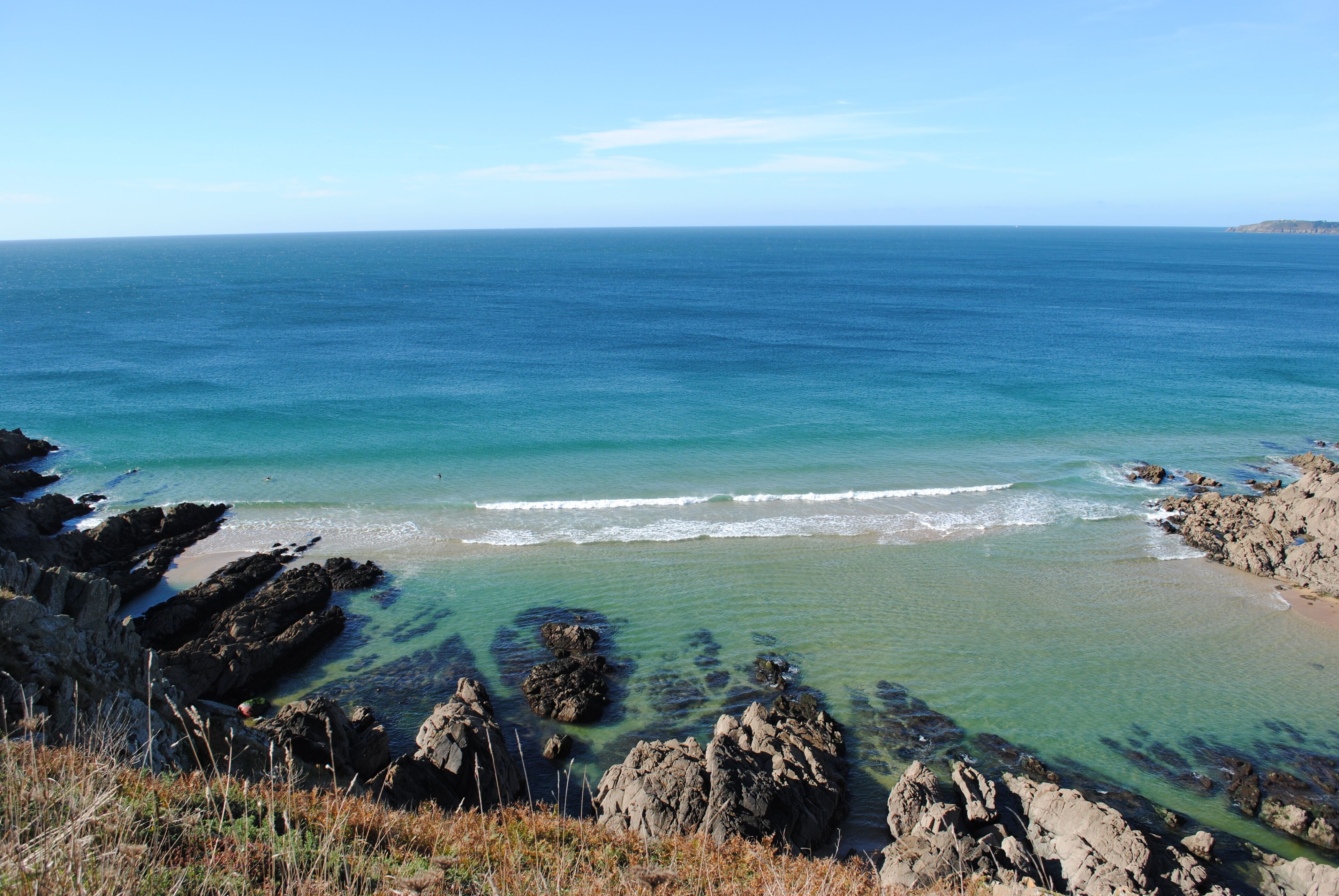 A coastal landscape with clear blue waters, rocky formations, and a distant shoreline.