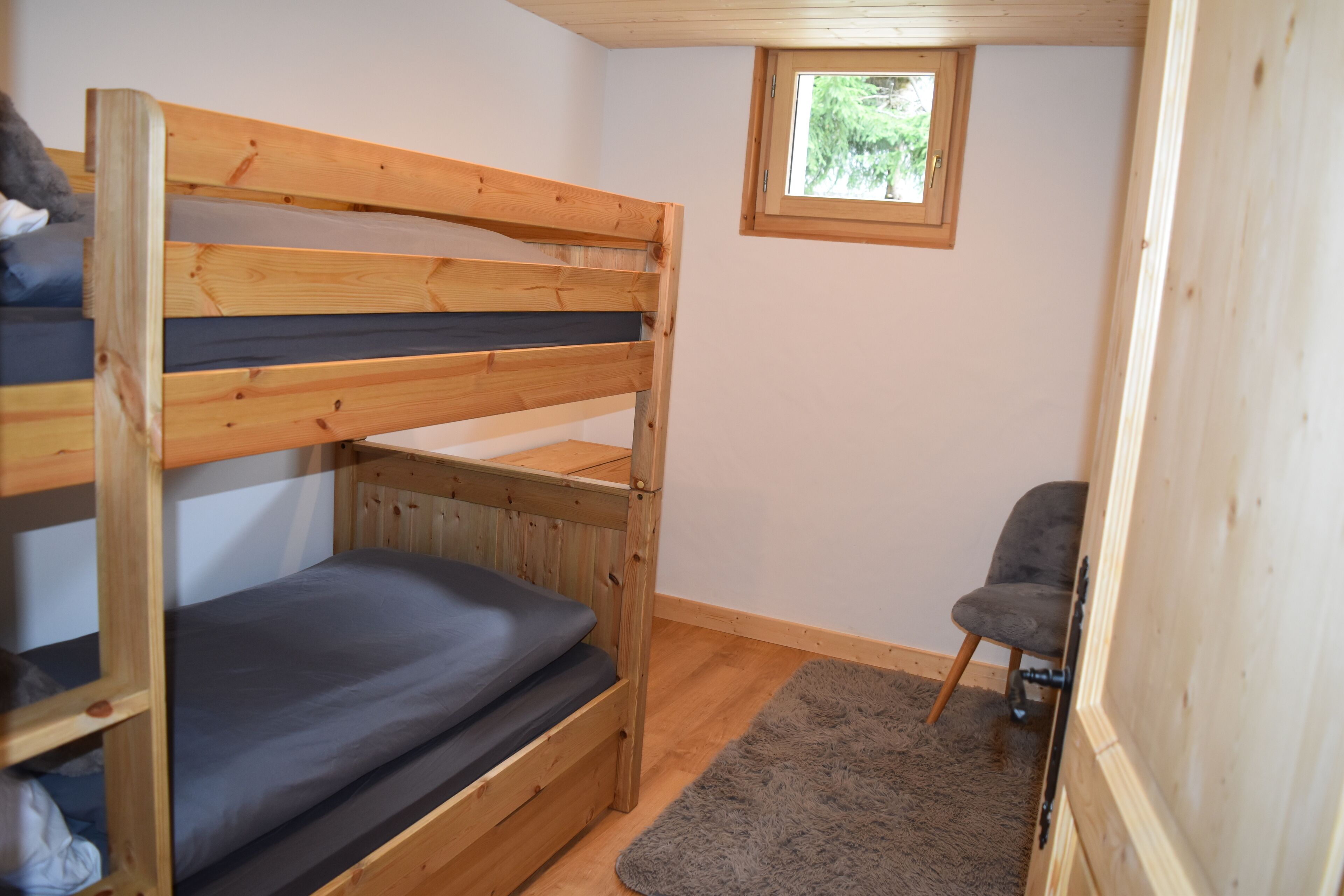 A bunk bed room with a small window, a chair, and a grey rug.