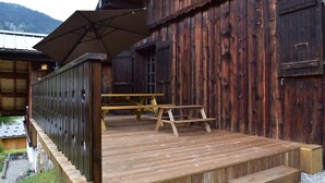 A wooden deck with a picnic table and benches, a large umbrella, and a rustic wooden building with a door and window. - Chalet with 4 bedrooms - 8 people - (Ideal Family, Group of friends) (Les Contamines-Montjoie)