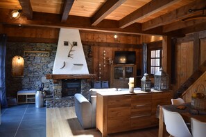 A rustic cabin interior with a stone fireplace, wooden beams, a stone wall, a television, and a dining area. - Chalet with 4 bedrooms - 8 people - (Ideal Family, Group of friends) (Les Contamines-Montjoie)