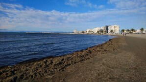 A beach with a sandy shore, a pier in the distance, and buildings along the coastline.