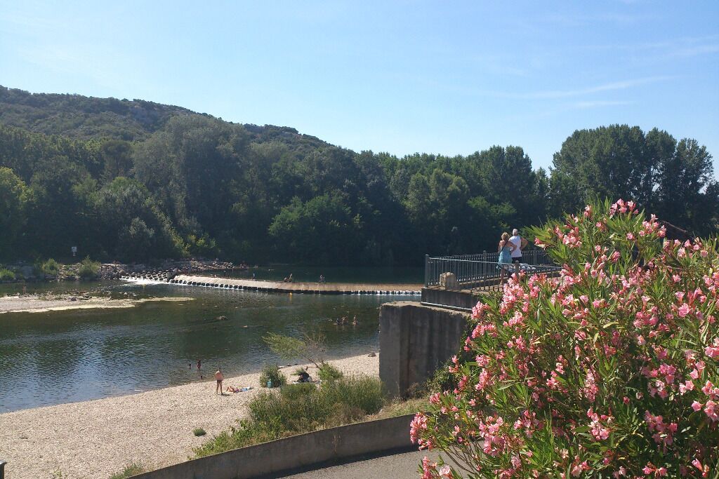 Un río con una pasarela de hormigón y un puente, rodeado de vegetación y colinas.