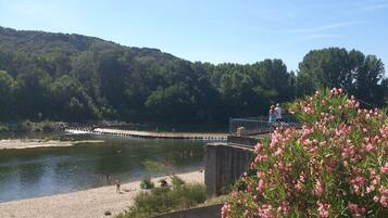 Un río con una pasarela de hormigón y un puente, rodeado de vegetación y colinas.
