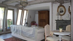 A room with a bed, a table with chairs, a chandelier, and a fireplace.
