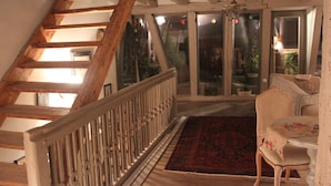 A wooden staircase with a white railing leading to a room with a floral tablecloth-covered table and a wicker chair.