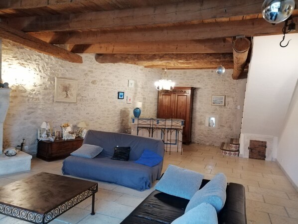 A rustic living room with exposed wooden beams, a stone wall, a blue sofa, a coffee table, and a chandelier.