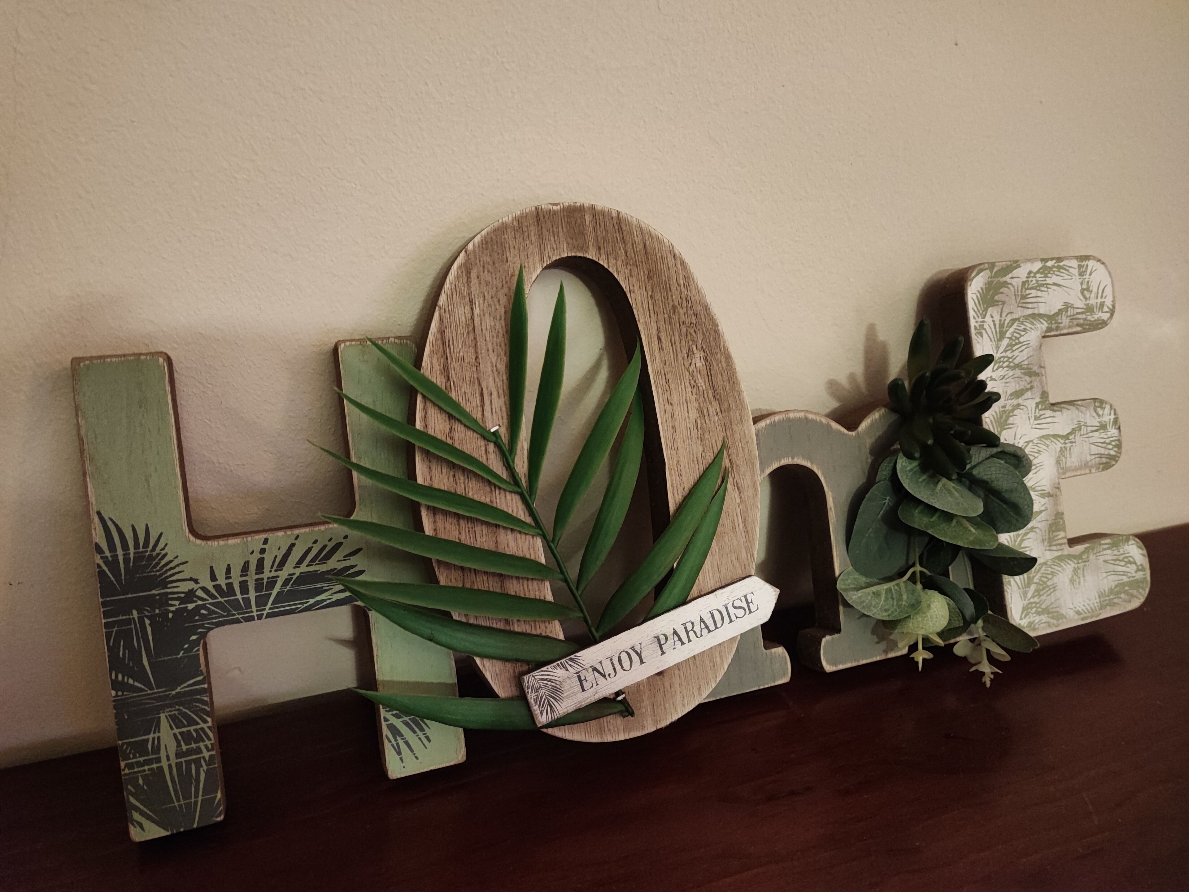 A decorative wooden sign with the word "HOME" and a small sign that reads "ENJOY PARADISE."