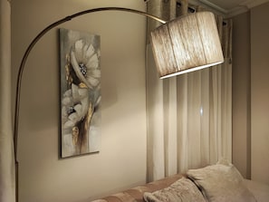 Ein Zimmer mit einer modernen Lampe, einem an der Wand befestigten abstrakten Gemälde und einem gemusterten Sofa.