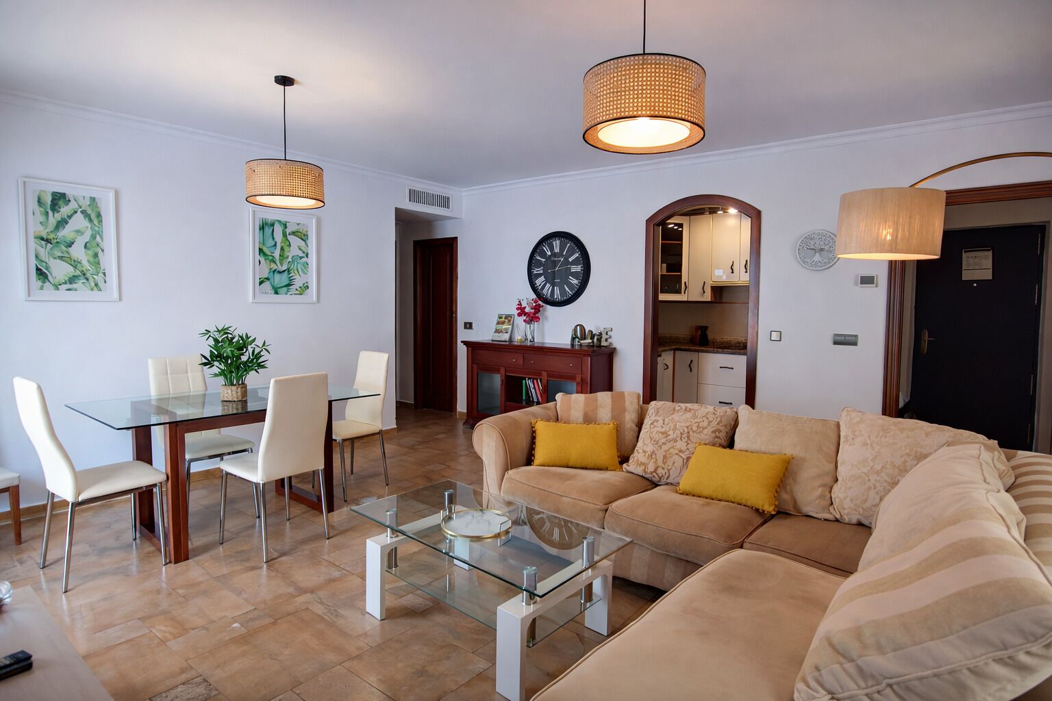 Una sala de estar con una mesa de centro de vidrio, un sofá color crema y dos lámparas colgantes.