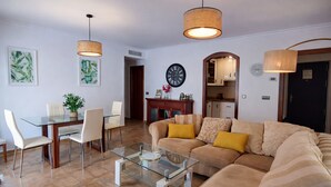Una sala de estar con una mesa de centro de vidrio, un sofá color crema y dos lámparas colgantes.