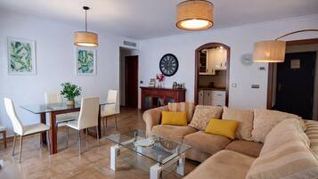 Una sala de estar con una mesa de centro de vidrio, un sofá color crema y dos lámparas colgantes.