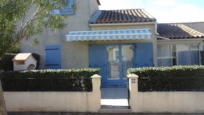 A two-story building with a tiled roof, a blue door, and a small porch.