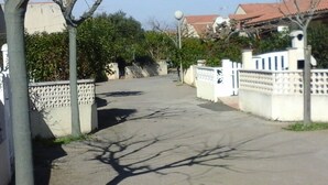 A paved driveway leading to a gated entrance with a white fence and decorative elements.